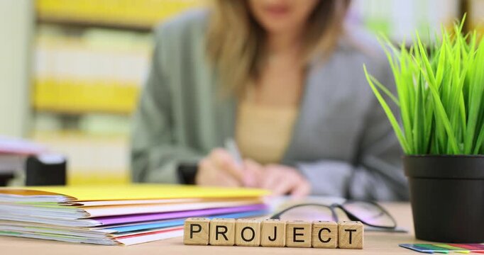 Businesswoman writes detailed plan for ambitious business project in notebook. Miniature wooden cubes form word Project on office desk. Slow motion