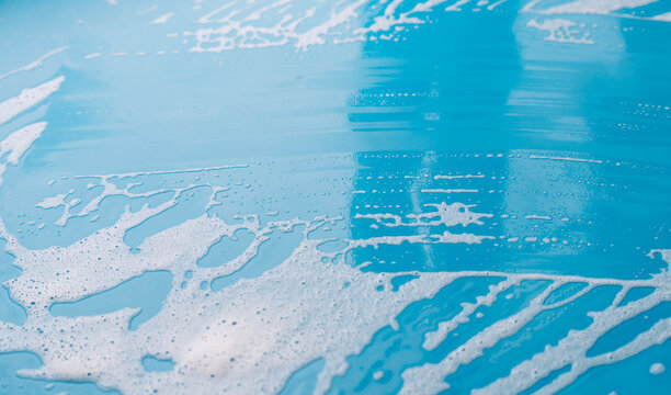 Broad cleared strip through cleaning foam on a blue surface with foamy edges.