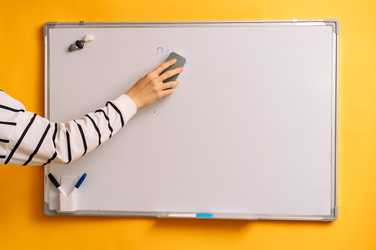 Hand erasing the word Plan from a whiteboard with a gray eraser.