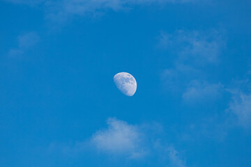 A Luminous Daytime Moon Floating in a Vast Blue Sky with Soft Clouds © Worawith
