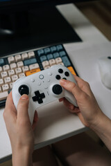Close-up of person hands holding using white video game controller while engaging in immersive gaming session sitting at desk, highlighting online entertainment, digital recreation, hobby. © dikushin