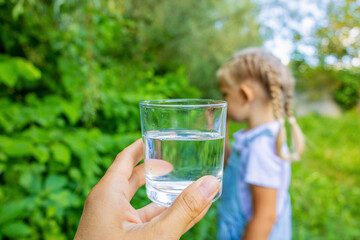 Fototapeta premium Little girl taking glass of clean water from adult hands in nature