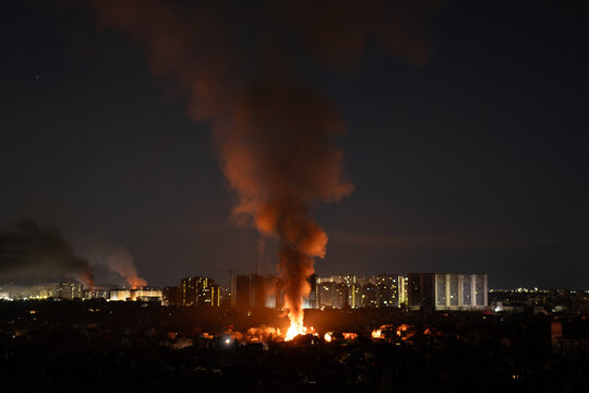 night city fire with thick smoke column rising over buildings panoramic view, urban fire aftermath with glowing flames and smoke plume at night, night cityscape with emergency fire event and smoke col