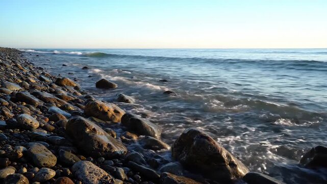 Pebbles on a rocky beach with gentle waves rolling in at golden hour with clear skies