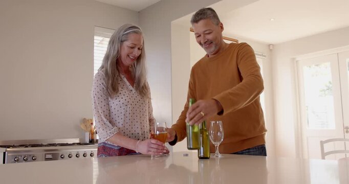 Sharing laughter and conversation, senior couple drinking wine in modern kitchen together