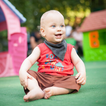 A cheerful baby sits on a soft green surface in a vibrant playground, surrounded by colorful play structures.