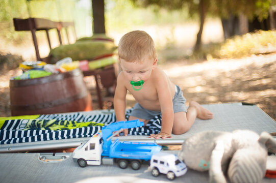 A young child enjoys a sunny day outdoors, crawling on a table surrounded by toy trucks and a soft companion. The peaceful setting invites laughter and joy.
