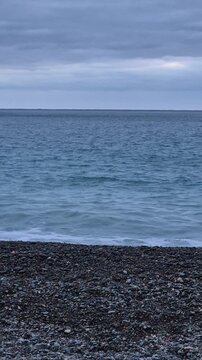 Lone swimmer explores tranquil sea waves at pebble beach during sunset, captured in a steady, fixed-position wide angle camera shot.