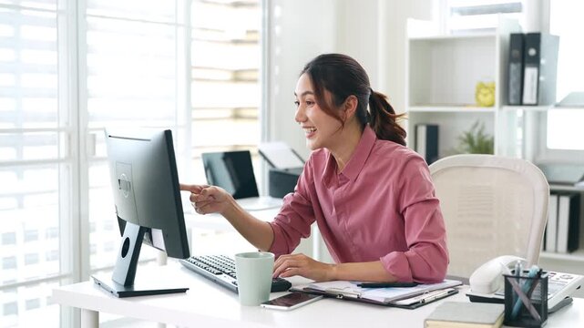 Asian business woman getting bonus reward, good news on pc computer at work in office. Happy, smiling ,winner, triumph, yes gesture.