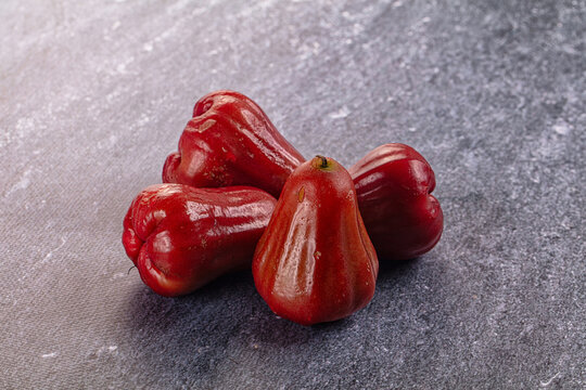 Four glossy red chompu fruits, also known as java apple or wax apple, arranged on textured gray surface with soft lighting and shallow depth of field