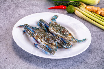 Fresh blue crabs on white plate with lemongrass, lime, chili and ginger on textured gray background © Andrei Starostin