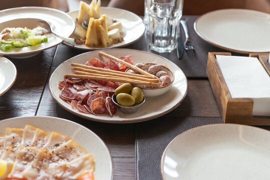 Elegant restaurant table setting with assorted charcuterie, olives, breadsticks, cheese and appetizers served on ceramic plates, creating a refined dining experience for lunch or dinner