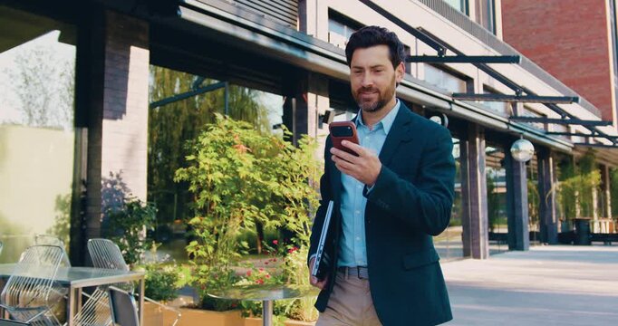 Businessman walking through city street using smartphone and responding to messages