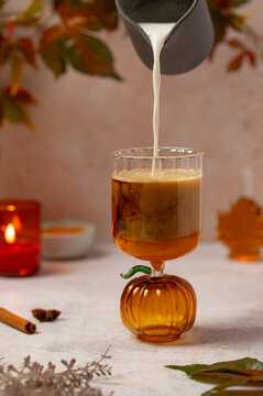 Pouring milk into a pumpkin-shaped glass with coffee and spices for autumn mood