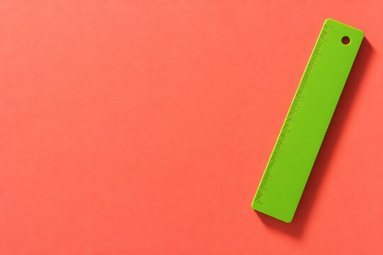 A bright green ruler is placed on a solid coral-orange background.