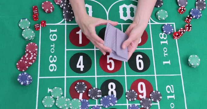 Woman dealer carefully shuffles thick deck of playing cards. Numerous bright casino chips rest on luxurious green roulette layout time lapse
