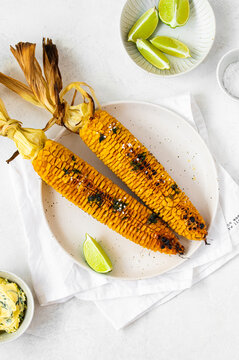Grilled sweet corn cobs with lime, salt, and herbs on a plate for summer barbecue.
