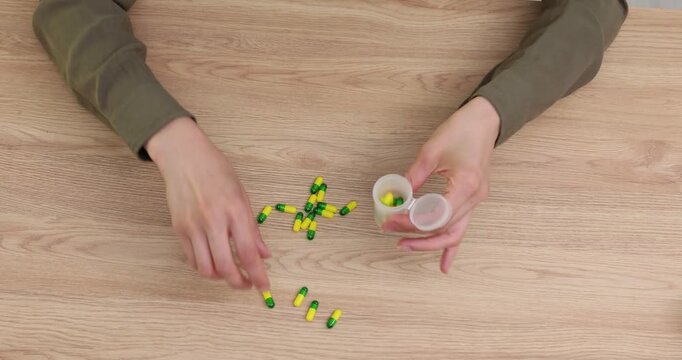 Woman pours handful of colorful tablets from small container onto table. Female places pills back into compact plastic container time lapse