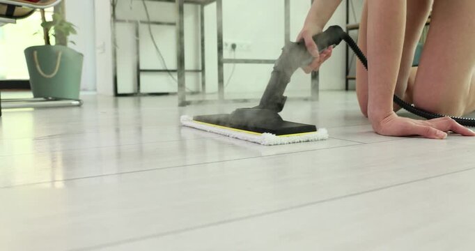 Woman cleans smooth floor with powerful steam cleaner. Housekeeper uses efficient handheld steam cleaner across laminate floor time lapse