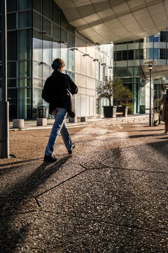 Pedestrian casting a long shadow in a modern office plaza in Paris, France, showing urban life and contemporary business architecture.