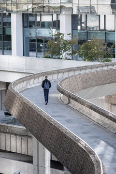 Person walking along a curved elevated walkway in Paris, France, within a contemporary business district of offices and urban infrastructure.