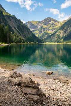 Scenic vertical view of Vilsalpsee lake with stones on the shore and alpine mountains