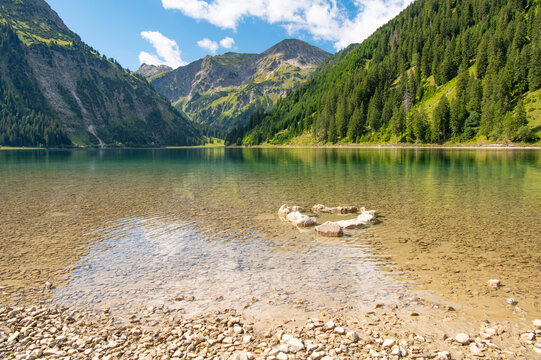 Crystal clear water of Vilsalpsee lake with stone heart formation and alpine mountains in Austria