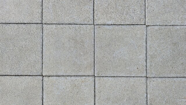 Grey square concrete paving blocks texture. Minimal grey stone paver wall and floor background. Top view grid pattern of outdoor concrete pavers on sidewalk floor.