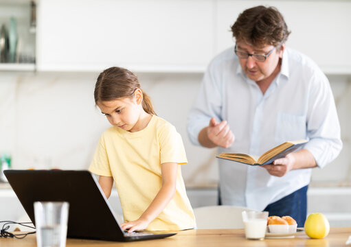 Father offers to read book to his daughter while she uses laptop