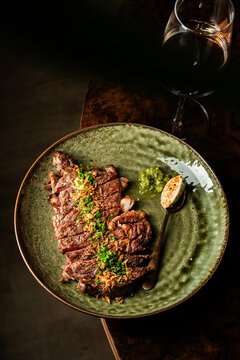 Sliced grilled beef steak with chimichurri sauce and compound butter, paired with a glass of red wine.