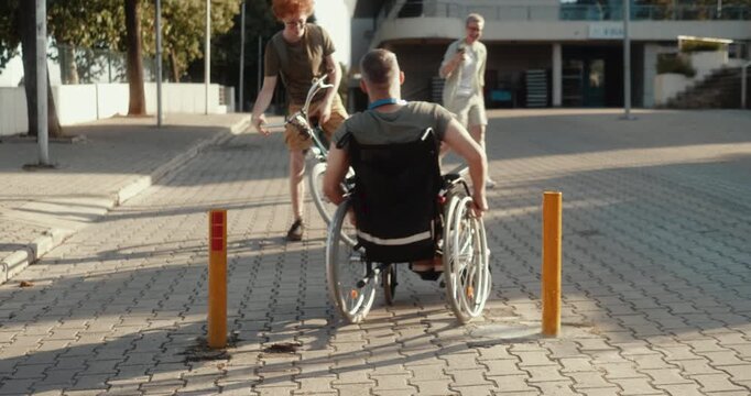 Two young friends enjoy a playful outdoor moment in an urban setting as a cyclist pulls a wheelchair user forward, capturing laughter, trust and social inclusion.
