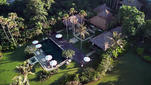 Luxury tropical resort villa with private swimming pool traditional thatched roof bungalows and lush green garden surrounded by palm trees in paradise orbit aerial drone footage
