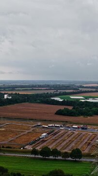 Vertical tracking shot moving left from steaming cooling tower and twin chimneys over harvested fields and truck parking under overcast sky in Niederaussem Germany