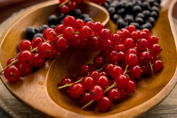 Macro view of juicy red currants and blueberries in a carved wooden bowl. Healthy organic food and summer berry concept. © YuliiaKettu