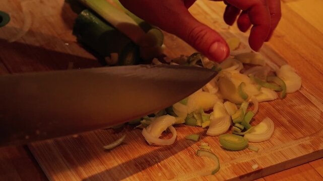 Chef chopping fresh leek on a wooden cutting board
