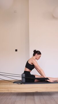 Pilates reformer training machine. woman practices pilates on reformer machine using attached straps for arm movements. Controlled resistance from springs supports strength and coordination.