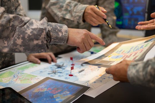 Experienced military hands focused intensely around a tactical map table, actively collaborating and planning precise strategic operations, operational logistics