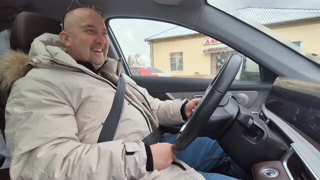 Man driving car through town while laughing during his daily commute on an overcast day. Side view medium shot.