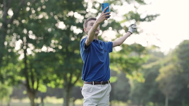 Young male golfer with a congenital amputation taking a selfie and talking to his smartphone on a beautiful sunny day at the golf course