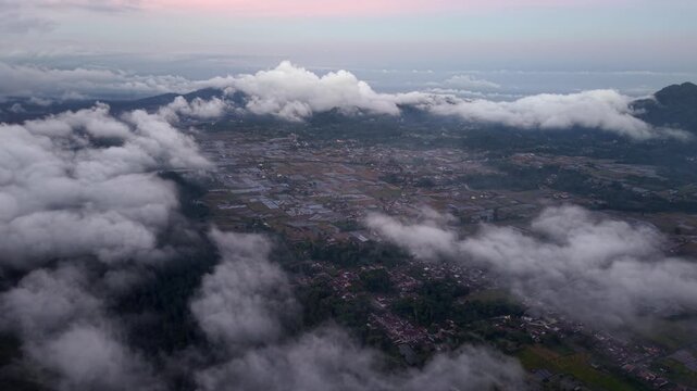 Clouds drift above misty mountains and valleys. Dense fog blankets towns and forests below at Pronojiwo, Lumajang