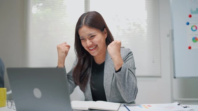 Young professional woman smiling while working on a laptop in a bright office, representing business, productivity, communication, and modern workplace success.