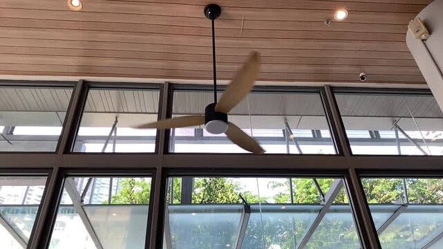 Slow motion shot of modern wooden ceiling fan spinning in bright room