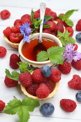 Fresh organic raspberries with tartlets, fresh green mint leaves, and purple cornflowers on white wooden background, sweet summer berry dessert © Andrii