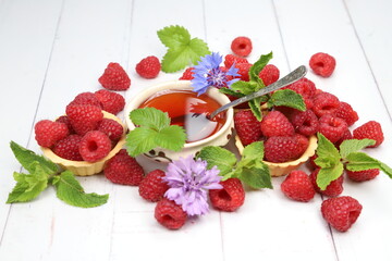 Fresh organic raspberries with tartlets, fresh green mint leaves, and purple cornflowers on white wooden background, sweet summer berry dessert © Andrii