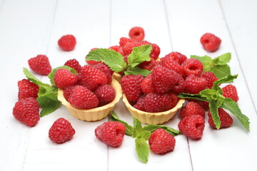 Fresh organic raspberries with tartlets, fresh green mint leaves, and purple cornflowers on white wooden background, sweet summer berry dessert © Andrii