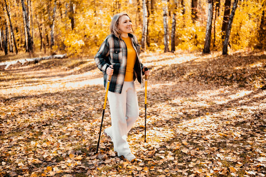 Active woman in autumn forest with nordic walking poles at fitness training. Fall outdoor sports and mental health improvement. Enjoying alone leisure time and escaping daily urban stress.