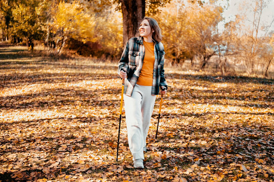 Energetic woman in autumn nature environment with walking sticks. Fall outdoor active lifestyle for mental health support. Escaping urban bustle for peaceful solo hiking through forest.