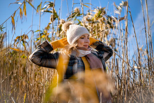 Relaxed woman in beanie enjoys autumn outdoor walk in pampas grass. Smiling female hiker stands in reed field under warm sunshine. Mindfulness, inner peace, mental health and burnout relief.