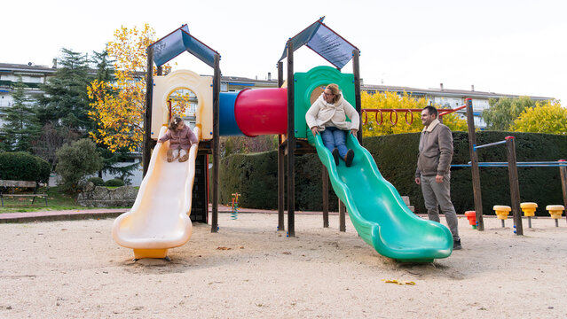 Family bonding playing on playground slides in autumn park