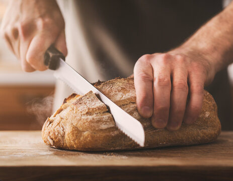 Hands slicing fresh bread loaf on cutting board